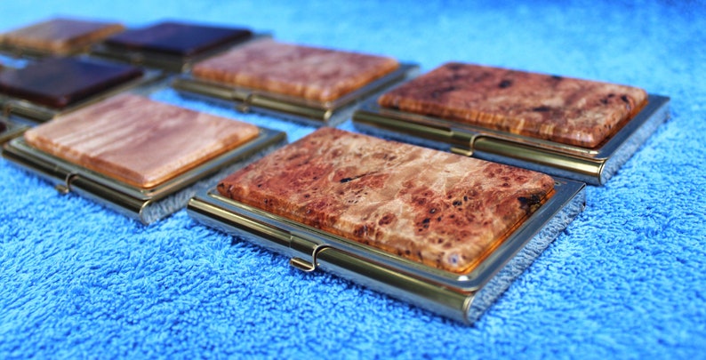 May include: A set of six wooden business card holders with a gold metal frame. The holders are made of different types of wood with unique grain patterns.