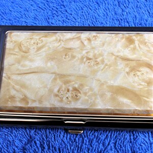 May include: A silver and gold metal business card holder with a white and brown marbled design.