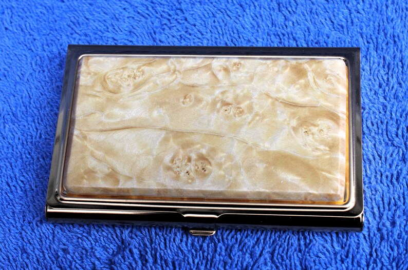 May include: A silver and gold metal business card holder with a white and brown marbled design.
