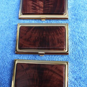 May include: Three gold-trimmed business card holders with a dark wood inlay. The wood has a swirling grain pattern.