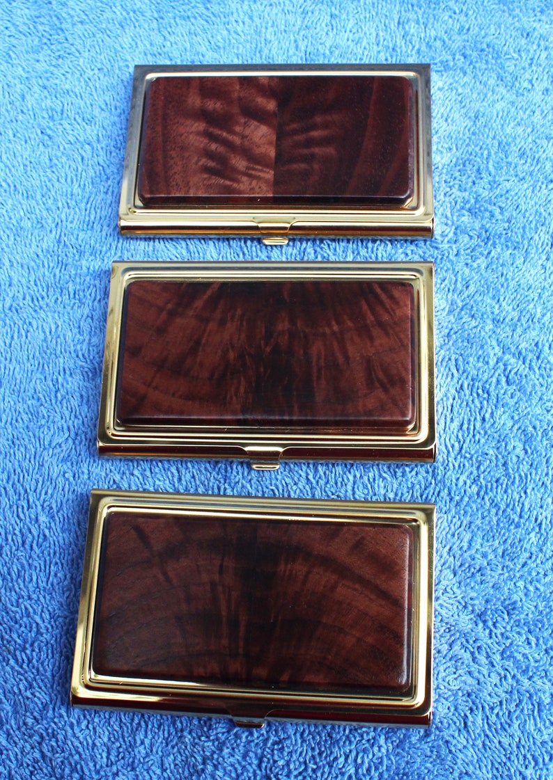 May include: Three gold-trimmed business card holders with a dark wood inlay. The wood has a swirling grain pattern.