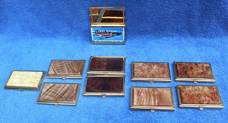 May include: Ten different wooden business card holders with gold trim. The holders are arranged in two rows of five. The holders are made of different types of wood, including maple, walnut, and cherry. The holders are all closed and have a gold hinge.