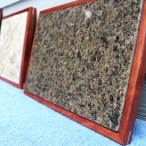 Puede incluir: Tres tablas de cortar enmarcadas en madera con diferentes superficies de granito. Las tablas están dispuestas horizontalmente con la tabla más grande en primer plano. Las tablas están sobre una toalla azul.