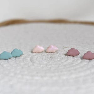 Puede incluir: Seis pendientes de botón con forma de nube en colores pastel. Hay pares de pendientes turquesa, rosa pálido y malva. Estos pendientes pequeños y delicados son adecuados para el uso diario. Los pendientes están hechos de un material liso.