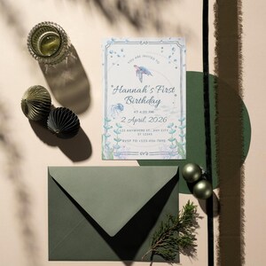 Könnte beinhalten: Einladungsset für einen ersten Geburtstag. Die Einladungskarte zeigt ein Unterwassermotiv mit einer Schildkröten- und Quallenillustration. Der Text lautet "Hannah's First Birthday" und enthält Datum, Uhrzeit und RSVP-Informationen. Das Set enthält einen grünen Umschlag und dekorative Elemente.