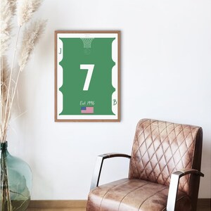 Puede incluir: Impresión enmarcada de una camiseta de baloncesto verde con el número 7 en blanco. La impresión incluye un gráfico de red de baloncesto, el texto "Est 1996" y una pequeña bandera estadounidense. El marco es marrón.