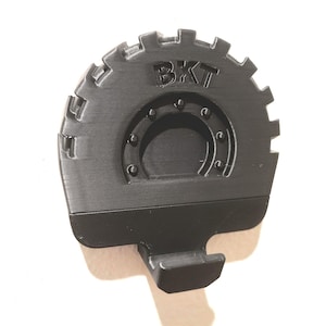 Może przedstawiać: Czarny, drukowany w 3D obiekt w kształcie opony z wytłoczonymi literami "BKT". Opona ma zębatą krawędź zewnętrzną i centralny okrągły wzór z nitami. Z dołu wystaje prostokątny haczyk.