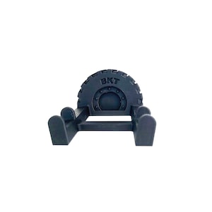 May include: A dark gray, stylized tire-shaped object with the letters "BKT" embossed on the top. The object has a circular design in the center and is supported by two curved legs on each side.