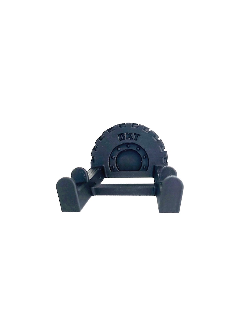 May include: A dark gray, stylized tire-shaped object with the letters "BKT" embossed on the top. The object has a circular design in the center and is supported by two curved legs on each side.
