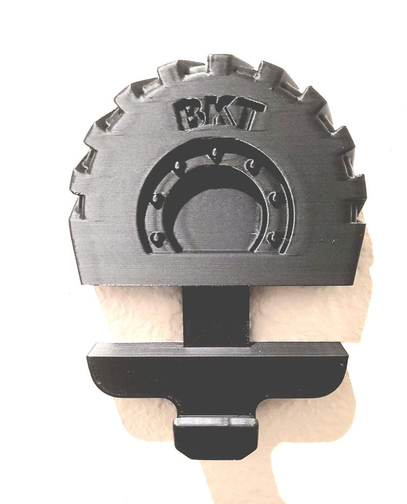 May include: A black, gear-shaped object with the letters "BKT" at the top. The object has a semi-circular design in the center and a rectangular base. The object is likely a mechanical part or component.