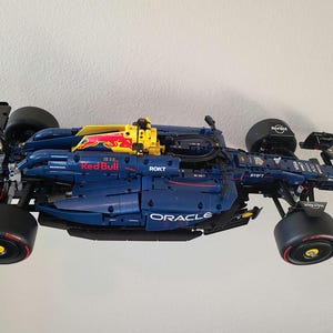 May include: A detailed model of a Formula 1 race car in dark blue, yellow, and black. The car features prominent Red Bull, Oracle, and ROKT branding, with black tires, a rear wing, and a complex aerodynamic body design constructed from building blocks.