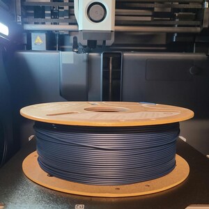 May include: A spool of dark blue filament sits inside a 3D printer. The printer has the text "Bambu Lab" on the print head. The build volume is 256 x 256 x 256 mm.