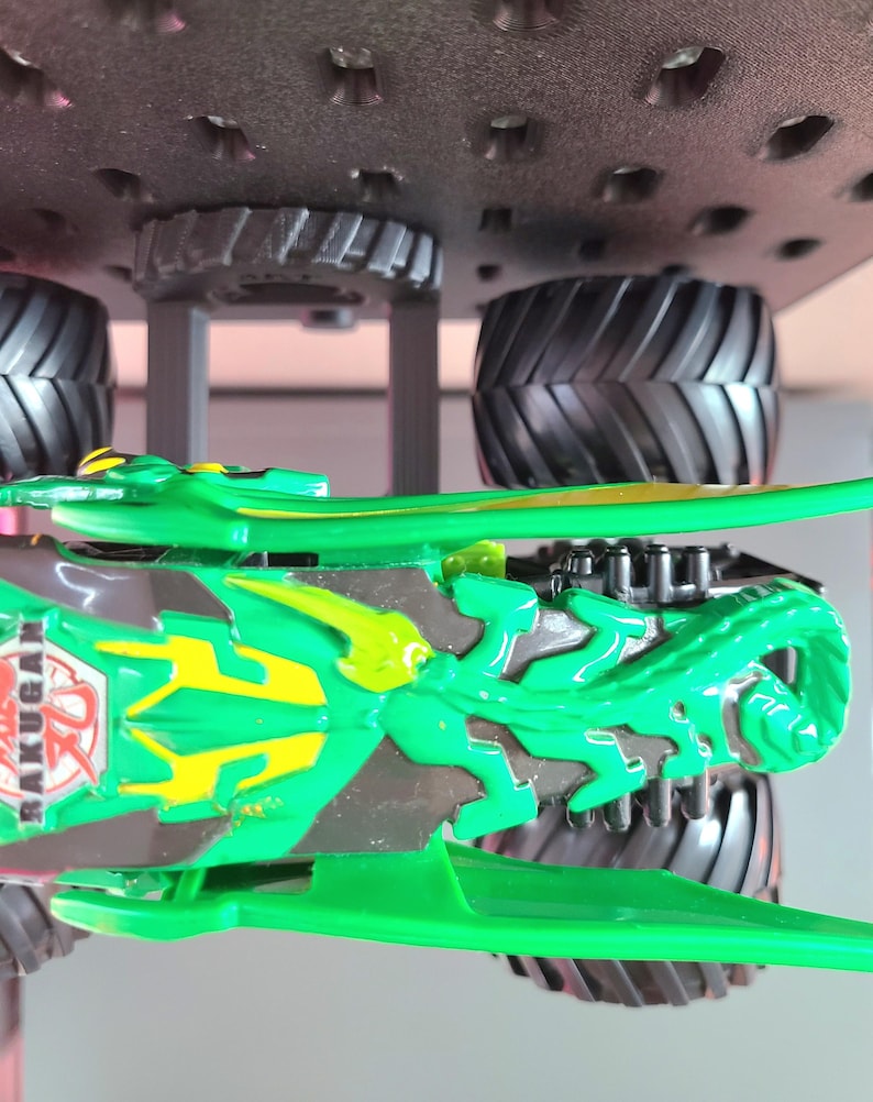 May include: Green and gray toy monster truck with large black tires. The truck features a detailed design with the word "BAKUGAN" visible on the side. The truck is designed with a green and yellow color scheme.
