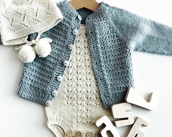 May include: A knitted baby outfit set in blue and white. The set includes a cardigan, a bodysuit, and a hat with pom-poms.