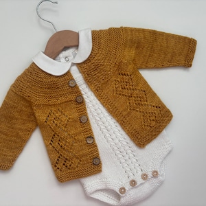 Può includere: Un cardigan di lana per neonato di colore giallo senape con un body bianco lavorato a uncinetto sotto. Il cardigan ha un colletto bianco e chiusura con bottoni.