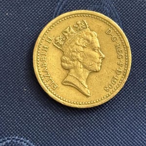 May include: A gold-coloured coin with a profile of a crowned head, the inscription "ELIZABETH II" and "D.G.REG.F.D.1993". The coin is circular with a textured edge. The coin is set against a blue background.