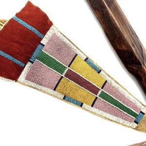 May include: A Native American-style beaded quiver with a dark red top and a geometric pattern in pink, yellow, green, and blue. The quiver is tan with a wooden handle.