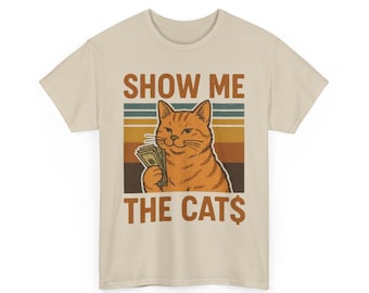 May include: Beige t-shirt featuring a cartoon cat holding money with the text "SHOW ME THE CATS" in brown and white. The cat is orange with a smug expression, set against a retro striped background.