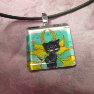 May include: Square pendant necklace featuring a black cat with yellow and green fairy wings. The cat is set against a teal background with gold accents. The pendant is attached to a black cord.