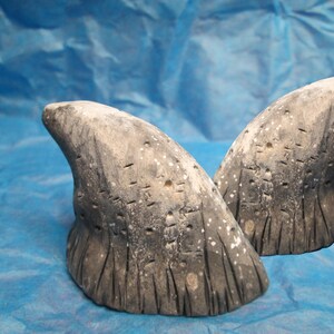 May include: Two gray, textured, ceramic, horn-shaped sculptures. The sculptures are slightly different in size and shape. The sculptures have a rough, uneven surface with a white, speckled pattern.