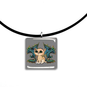 May include: A square pendant necklace featuring a cartoon cat with teal and gold wings. The cat has large green eyes and is set against a gray background. The pendant hangs from a black cord.