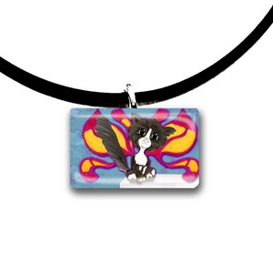 Puede incluir: Un collar de gargantilla negro con un colgante rectangular que presenta un gato de dibujos animados con pelaje blanco y negro, ojos verdes y una larga cola. El fondo tiene un diseño azul, naranja y rosa.