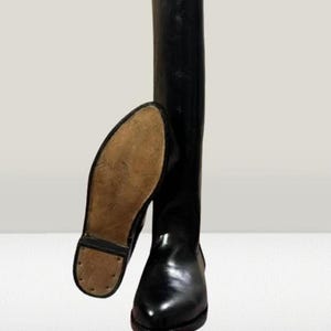 May include: A pair of black leather riding boots. One boot is upright, the other is lying on its side, showcasing the sole. The boots have a glossy finish and a classic design, suitable for equestrian activities.