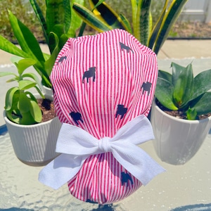 May include: A pink and white striped scrub cap with a pattern of black bulldog silhouettes. The cap is tied with a white bow. The cap is designed for medical professionals.