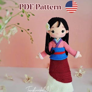 May include: A crocheted doll in a traditional outfit, featuring a pink top, blue sash, and a long red skirt. The doll has black hair, a white flower, and is labeled "PDF Pattern". The image includes the American flag.