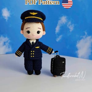 May include: A crocheted pilot doll wearing a navy blue uniform with gold accents and a matching hat. The doll is holding a small black suitcase. The image includes the text "PDF Pattern" and a US flag.