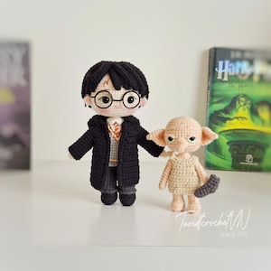 May include: Crocheted Harry Potter and Dobby dolls. Harry wears a black coat, glasses, and has a lightning bolt scar. Dobby is beige and holds a gray item. The text "TuoidtcrochetN SINCE 2023" is visible.