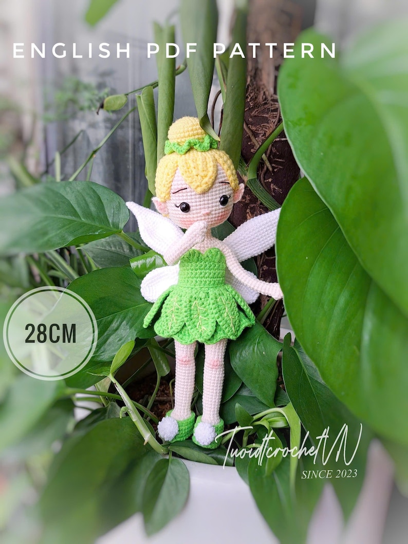 May include: A handmade crochet fairy doll, approximately 11 inches tall, with a green dress, yellow hair, and white wings. The doll is surrounded by green foliage. The text "ENGLISH PDF PATTERN" is visible at the top.