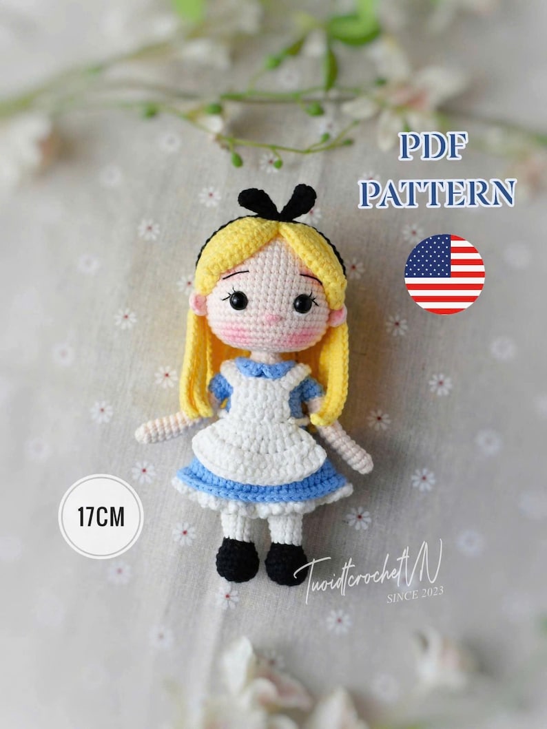 Puede incluir: Mu&ntilde;eca de ganchillo de un personaje con cabello rubio, un lazo negro y un vestido azul y blanco. La mu&ntilde;eca mide aproximadamente 17 cm de alto. La imagen incluye el texto "PDF PATTERN" y una bandera estadounidense.