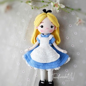 May include: A handmade crochet doll of Alice in Wonderland. The doll has yellow hair, a blue dress with a white apron, and black shoes. The doll is made with a crochet stitch and has a sweet, innocent expression.