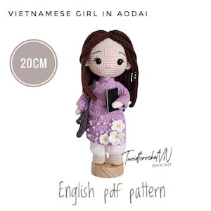 May include: A handcrafted crochet doll depicting a Vietnamese girl in an Ao Dai. The doll is approximately 7.9 inches tall, with brown hair and a purple outfit adorned with white flower accents. The image includes text that reads "Vietnamese Girl in Ao Dai" and "English pdf pattern."