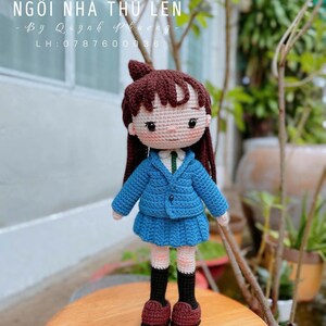 Pode incluir: Boneca de croch&ecirc; feita &agrave; m&atilde;o, vestindo uniforme escolar azul, saia combinando e sapatos bord&ocirc;. A boneca tem cabelo castanho e est&aacute; em uma superf&iacute;cie de madeira. Os textos "NG&Ocirc;I NH&Agrave; TH&Uacute; LEN" e "MADE BY OUR LOVELY CUSTOMER" s&atilde;o vis&iacute;veis.