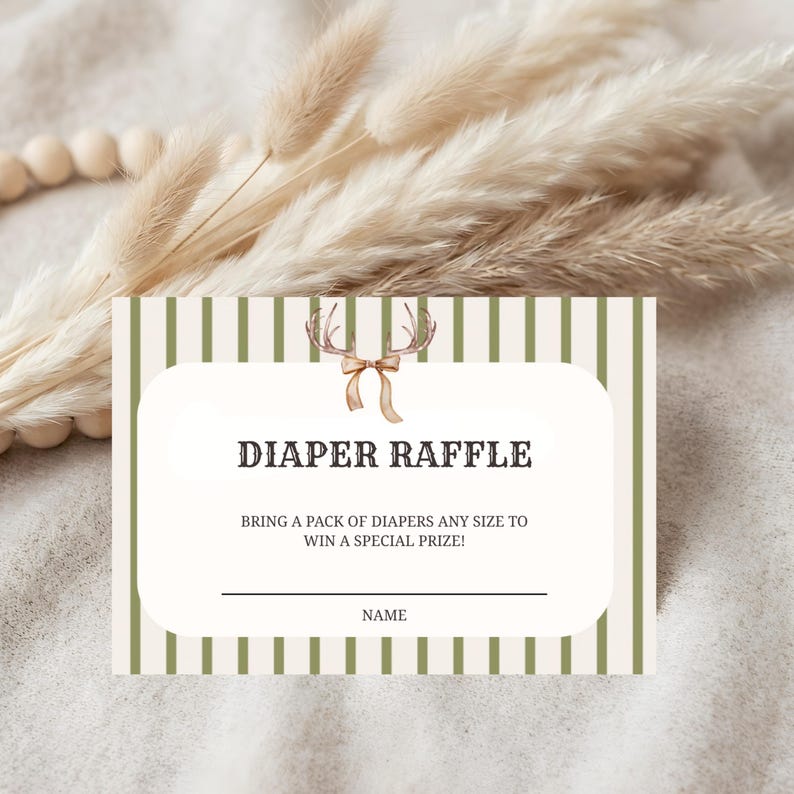 May include: A rectangular diaper raffle card featuring a white center panel with a brown deer antler and ribbon graphic. The card has olive green and white vertical stripes on the sides and includes the text: DIAPER RAFFLE, BRING A PACK OF DIAPERS ANY SIZE TO WIN A SPECIAL PRIZE!, and a line for a NAME.