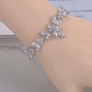 May include: Silver bracelet with a floral design, adorned with clear, sparkling crystals. The bracelet includes a delicate chain for adjustable sizing. The crystals are arranged in a leaf-like pattern, creating an elegant accessory.