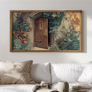 Può includere: Una stampa incorniciata raffigura una porta di legno socchiusa, incastonata in un muro di pietra e circondata da vegetazione. L'opera d'arte presenta una calda tavolozza di colori con sfumature di marrone, verde e arancione, creando un'estetica vintage.