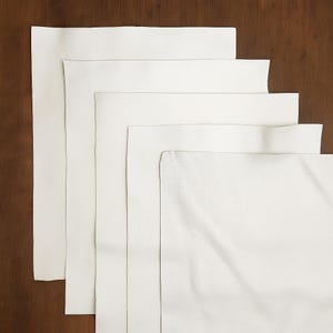 May include: A stack of white leather sheets of varying sizes, arranged on a dark brown wooden surface. The leather appears smooth and pristine, with subtle variations in texture. The sheets are rectangular, with clean edges.