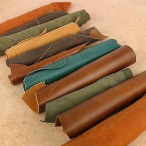 May include: A collection of rolled leather hides in various colors, including shades of brown, green, and tan. The hides are arranged diagonally, showcasing their textures and tones. The image highlights the natural variations in the leather.
