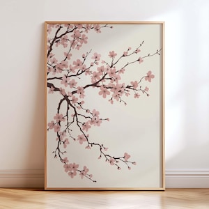 Pode incluir: Uma impressão de arte emoldurada com um galho de flores de cerejeira. As flores são rosa suave e os galhos marrons escuros contra um fundo creme. A moldura é de cor de madeira clara.