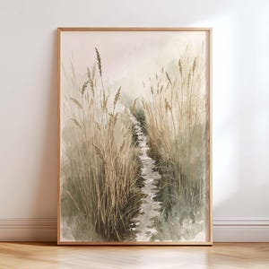 May include: A framed watercolour print depicting a tranquil landscape. The artwork shows tall, dried grasses bordering a narrow stream, rendered in muted tones of beige, green, and grey. The frame is light brown. The image conveys a sense of peace and natural beauty.