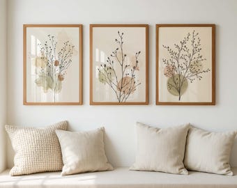 May include: Three framed botanical art prints. Each print features a branch with small leaves and berries, set against a soft, neutral background with muted colour washes. The frames are a warm, natural wood tone. The prints are displayed above cushions.