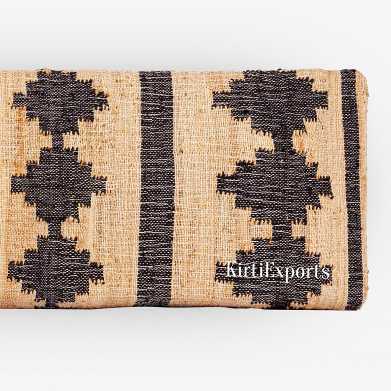 Puede incluir: Un tejido rectangular con un patr&oacute;n repetitivo de formas geom&eacute;tricas de diamante en negro y rayas verticales sobre un fondo beige natural. La tela tiene una textura gruesa visible e incluye el texto en blanco KirtiExports.