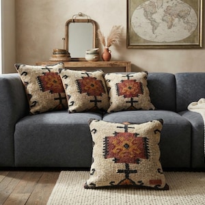 Könnte beinhalten: Vier quadratische Dekokissen mit einer strukturierten cremefarbenen Basis und einem markanten geometrischen Muster in Rost-, Orange- und Dunkelgrautönen. Die Kissen sind auf einem dunkelgrauen Sofa angeordnet, eines liegt im Vordergrund auf dem Boden.