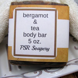 May include: A brown and white bar of soap with a label that reads "bergamot & tea body bar 5 oz. PSR Soapery".