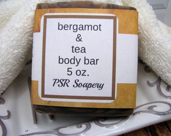 May include: A brown and white bar of soap with a label that reads "bergamot & tea body bar 5 oz. PSR Soapery".