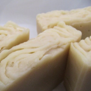 May include: Four bars of white soap with a swirl pattern. The soap is arranged in a row on a white surface.