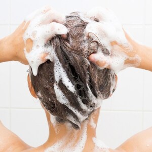 May include: A person with brown hair is washing their hair in the shower. The hair is covered in white shampoo suds.